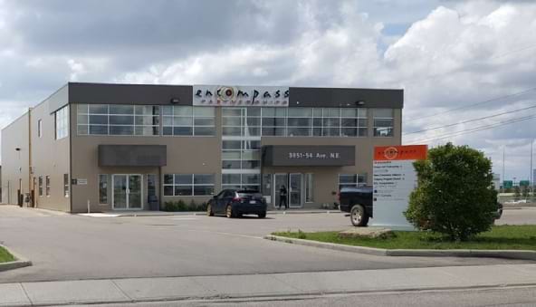 Front view of the
            Encompass Partnerships building, a two-story structure with large
            glass windows, located in a parking area under a partly cloudy sky.