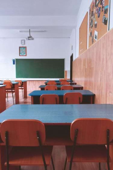 Empty classroom with orange chairs, wooden desks, and a green chalkboard.