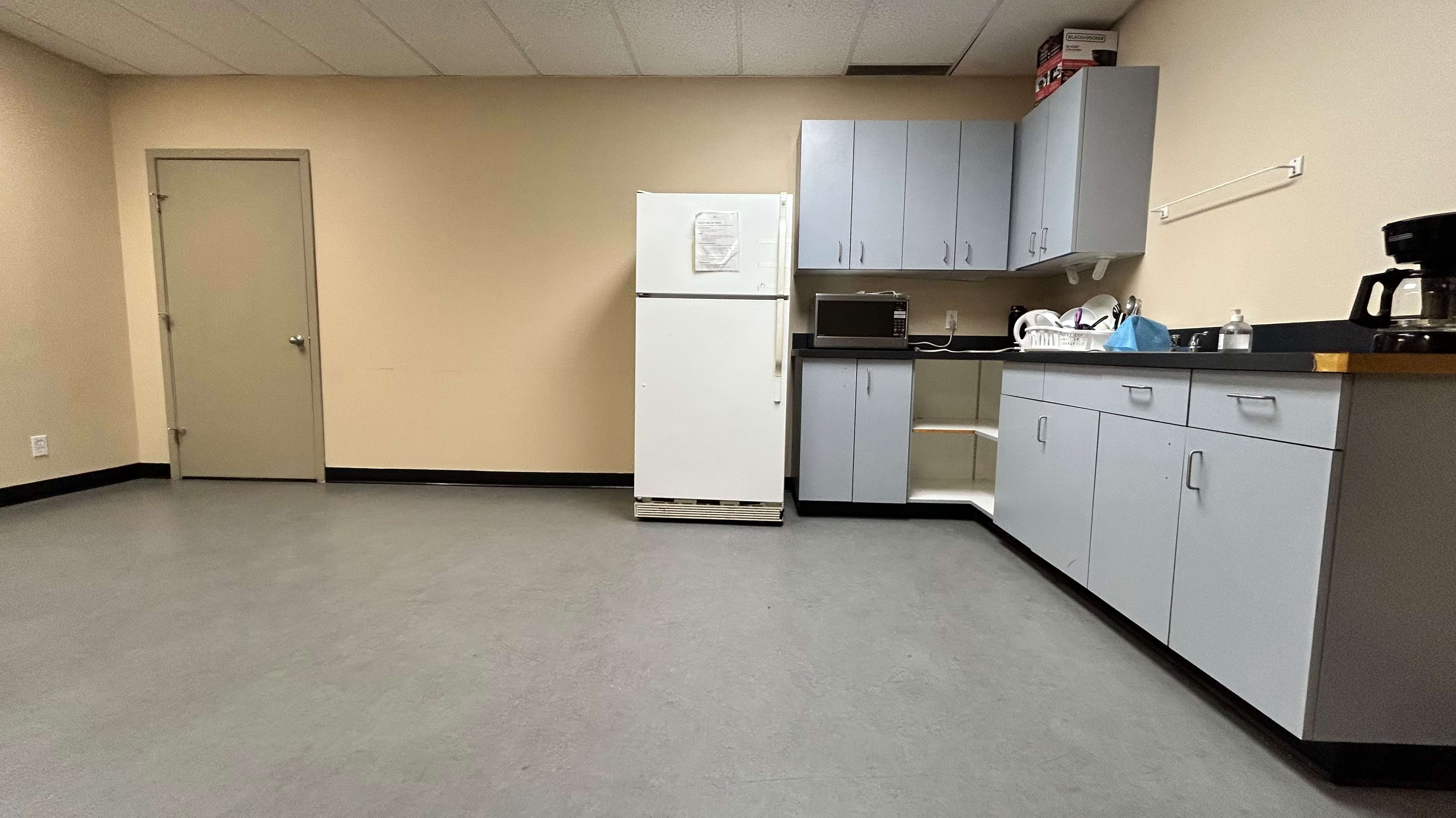 A sparsely equipped office kitchenette with cabinets, a fridge, and a microwave.