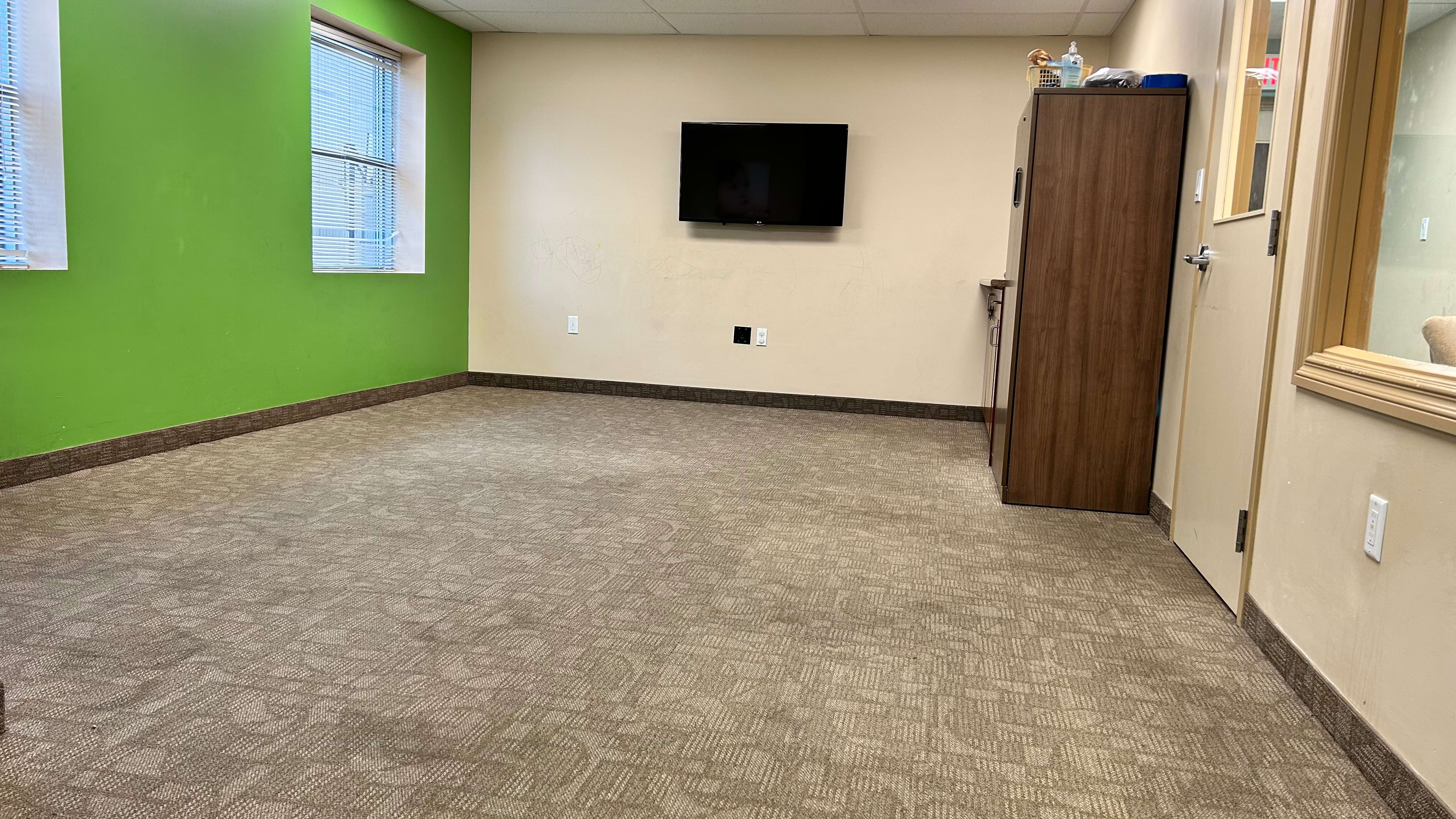 Empty office room with green and beige walls, a window, and a mounted TV.