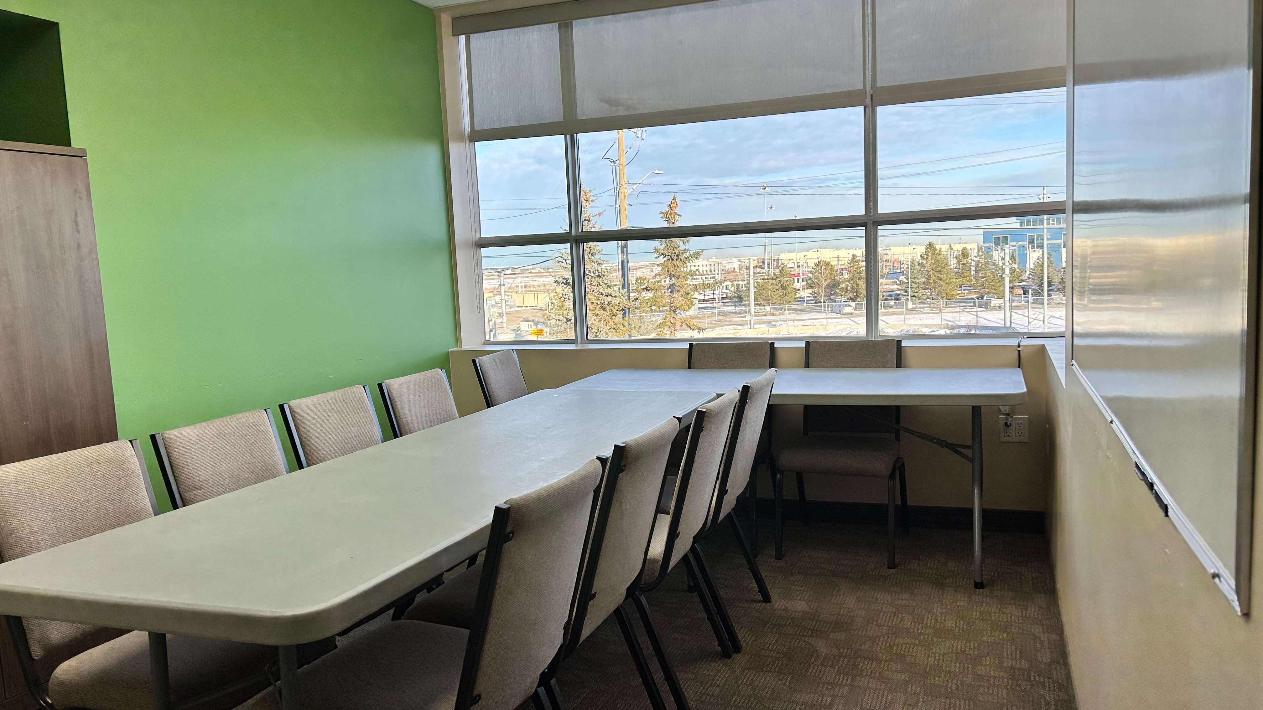 Empty meeting room with large table, chairs, and window view of urban landscape.