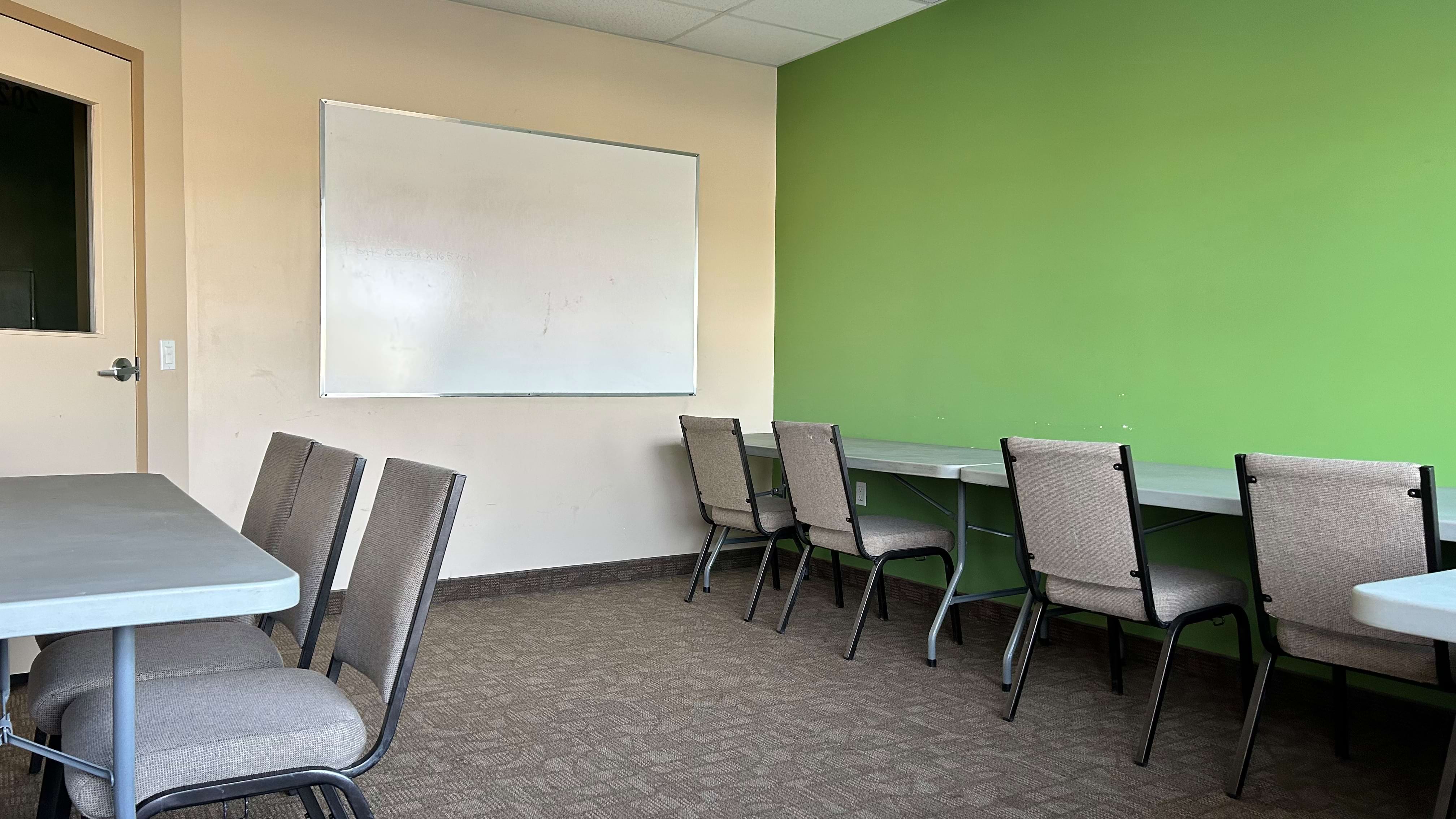 A meeting room with tables, chairs, a whiteboard on the wall, and a green accent wall.