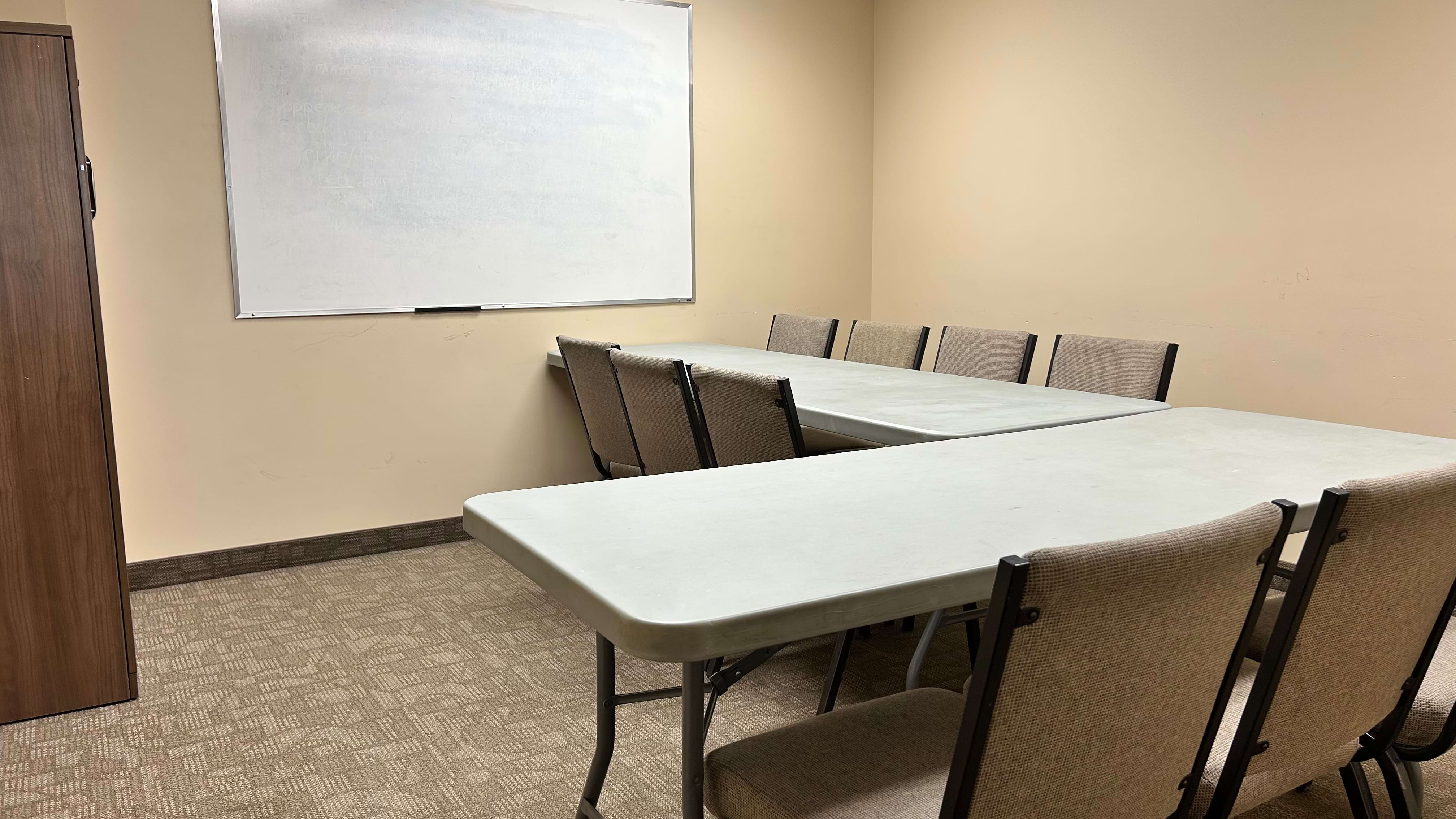 A meeting room with tables, chairs, and a whiteboard on the wall.