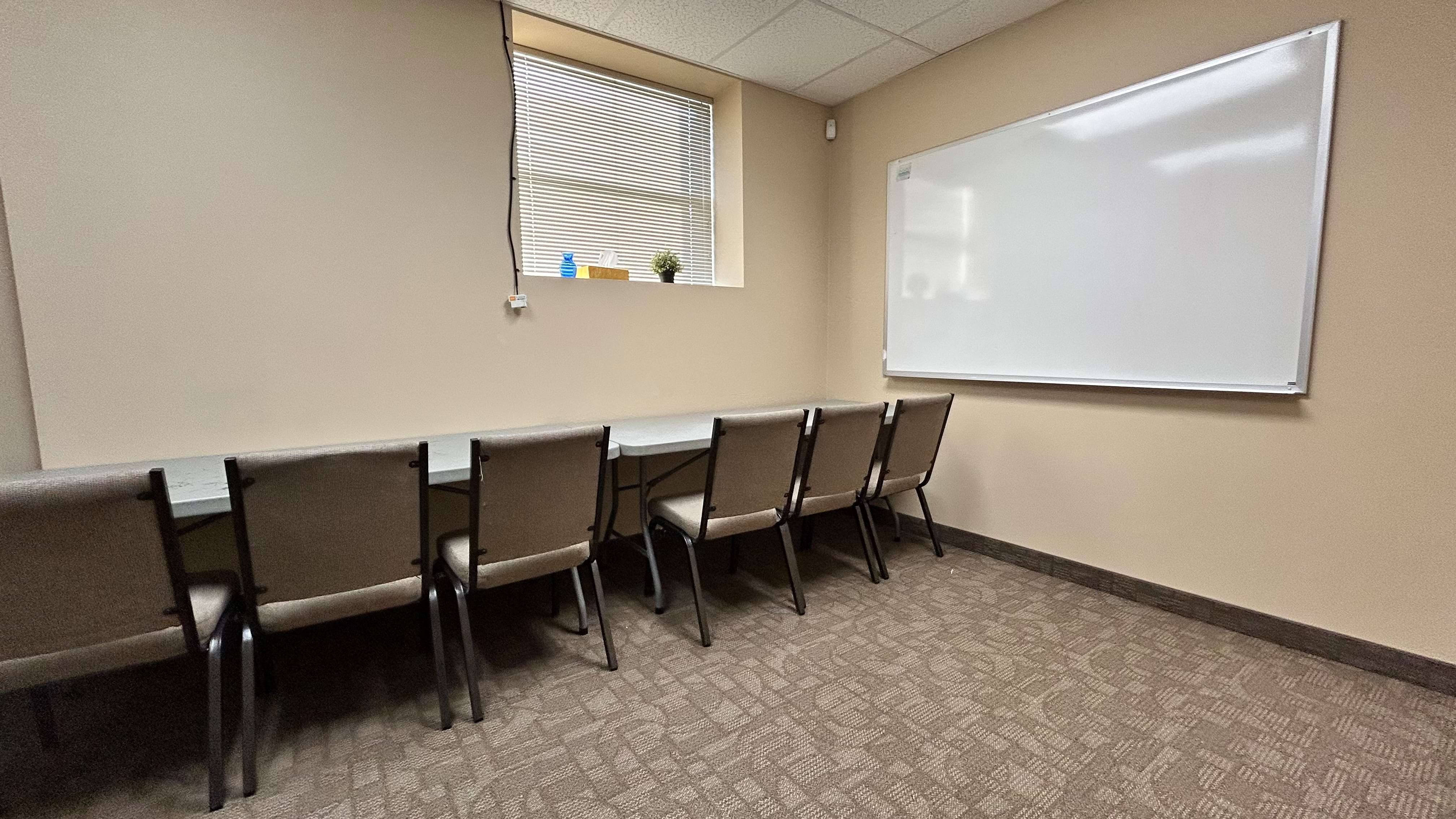 A conference room with a long table, chairs, a whiteboard and a window with blinds.